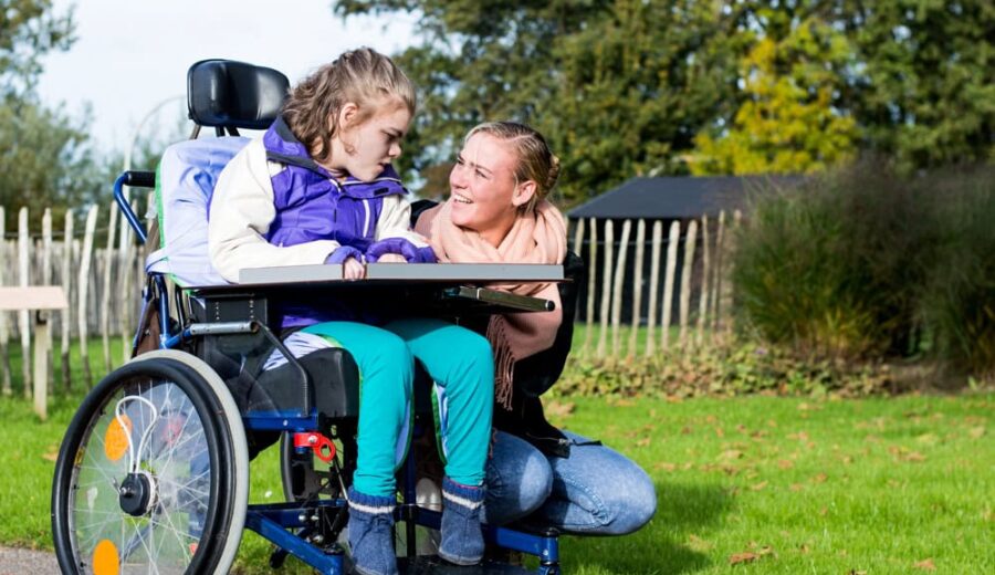Meisje in rolstoel met zorgverlener ernaast